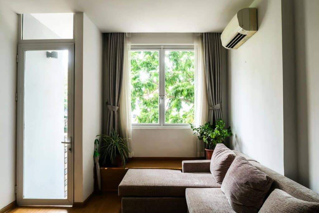 Bright living room with a cozy sofa, indoor plants, and a large window with curtains.